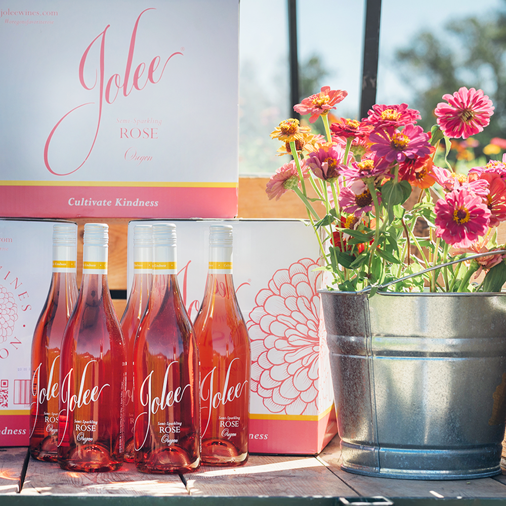 five bottles of Jolee Rose next to case boxes and tin bucket with zinnias