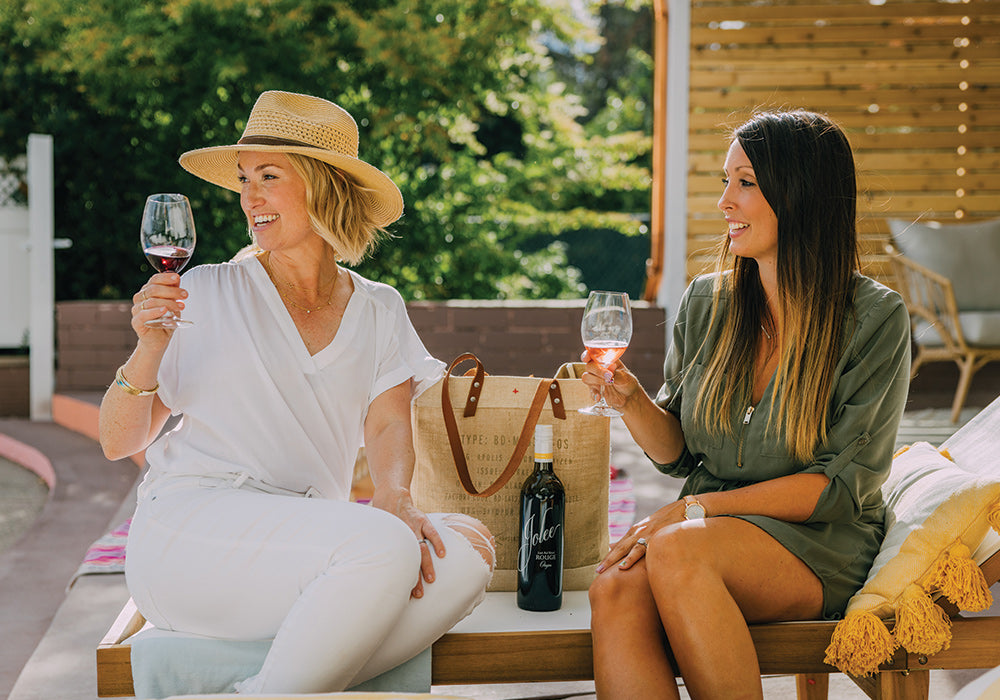 two ladies holding wine glasses and a bottle of jolee wine in between them.
